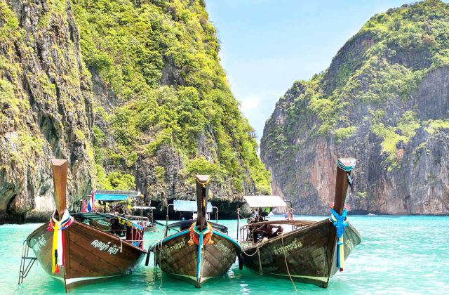 Barcos tradicionales de cola larga sobre las aguas turquesas de Maya Bay, entre acantilados cubiertos de vegetación, en Tailandia