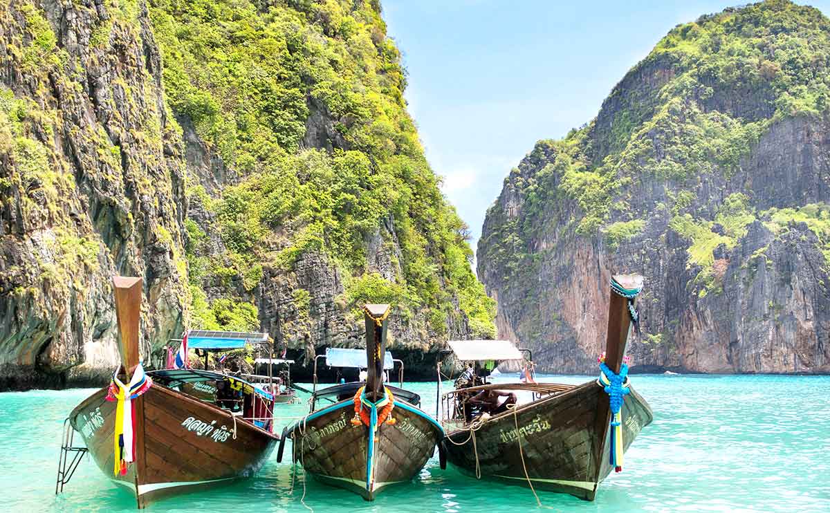 Barcos tradicionales de cola larga sobre las aguas turquesas de Maya Bay, entre acantilados cubiertos de vegetación, en Tailandia