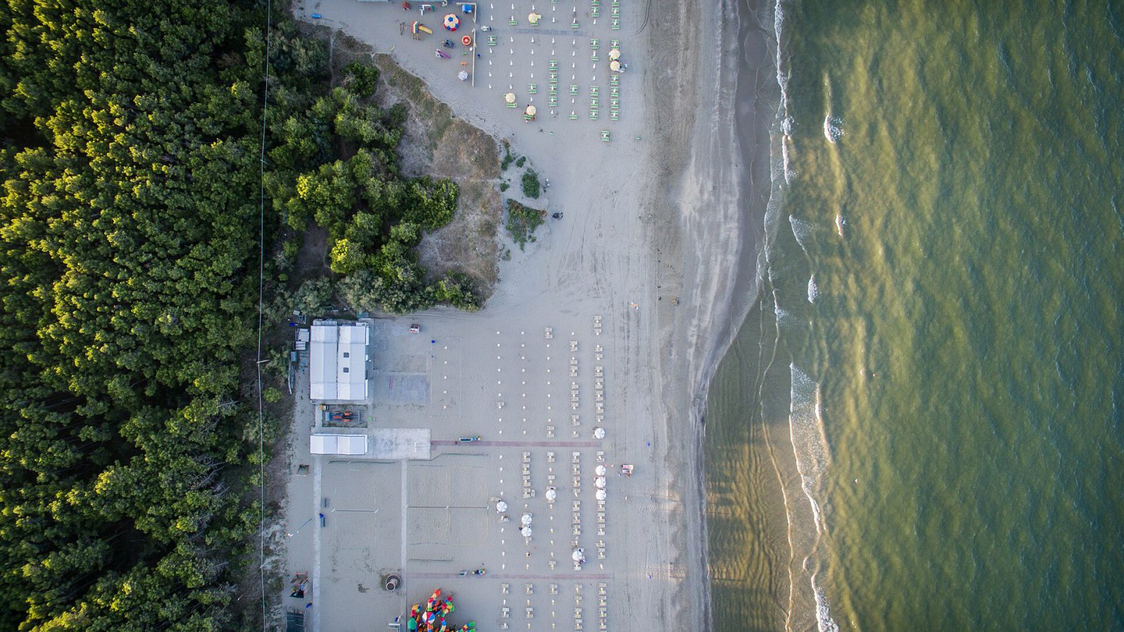 Vista aérea de una playa casi vacía de la costa de Rávena, Italia, con las sombrillas cerradas, junto al mar y un pinar