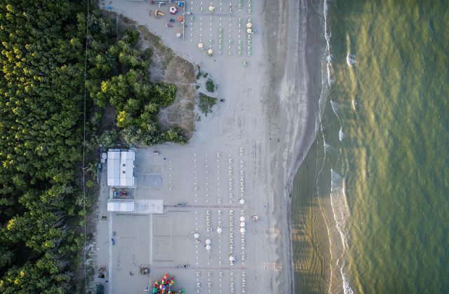 Vista aérea de una playa casi vacía de la costa de Rávena, Italia, con las sombrillas cerradas, junto al mar y un pinar